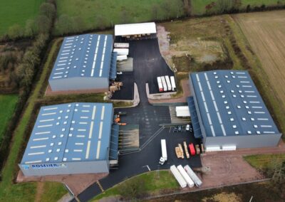 Vue aérienne de deux grands entrepôts industriels avec des camions et des remorques garés à l'extérieur, entourés de champs.
