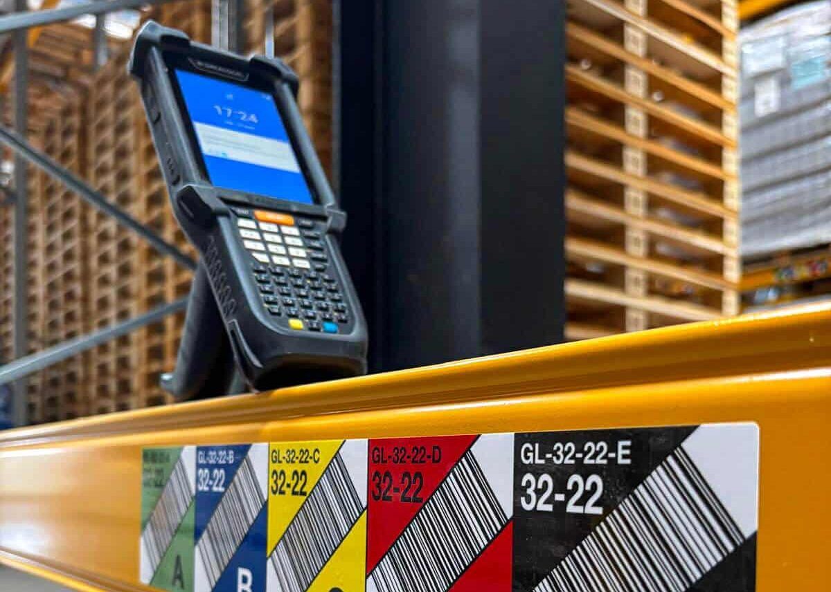 wms-performant Un scanner portatif repose sur une étagère d'entrepôt étiquetée avec des codes-barres colorés et les lettres de section A à E.